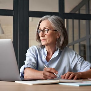 mature-woman-looking-at-laptop-and-taking-notes