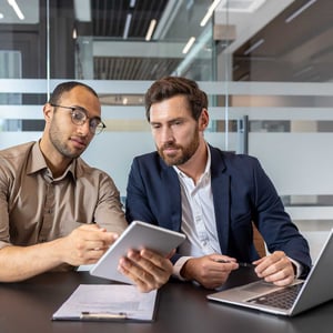 two-businessmen-reviewing-a-tablet-and-laptop